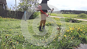 Person gardener mows tall green grass, holding in manly hands, gasoline lawn mower, weeds flying in different directions