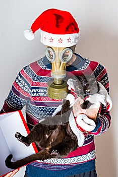 Person in gas mask against Covid-19 in Christmas hat taking of the black cat of the Christmas box