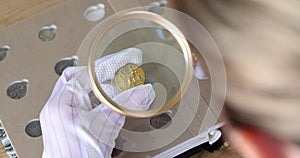 Person in gloves looks at coins through magnifying glass