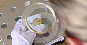 Person in gloves looks at coins through magnifying glass