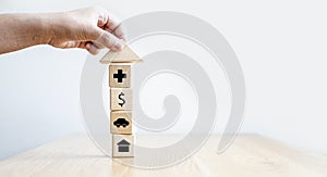 A person grabs a triangular roof-shaped wooden block on top of a rectangular wooden block with icons.