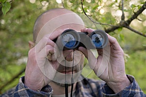 person in green bushes observes object through binoculars, espionage, covert surveillance operation, thrill-seeker tracks down photo