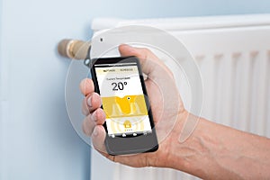 Person hand adjusting temperature of thermostat using cellphone