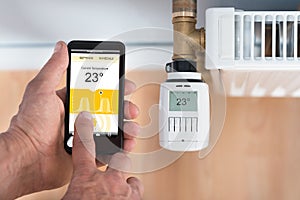 Person hand adjusting temperature of thermostat using cellphone