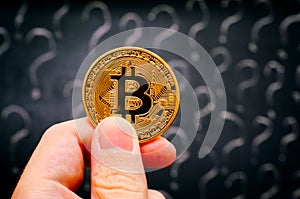 Person hand with Bitcoin virtual money against blackboard with question marks