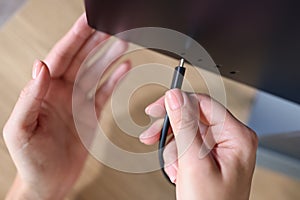 Person hand connects a black USB-C or Type C power cable to computer