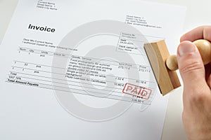 Person hand holding rubber stamp over paid invoice