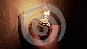 Person Hand Inserts a Flickering Light Bulb, a Night Light into a Socket on Wall