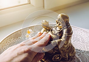 Person hand rubbing small golden laughing Buddha figurine tummy. It believed to bring happiness, good fortune and wealth.