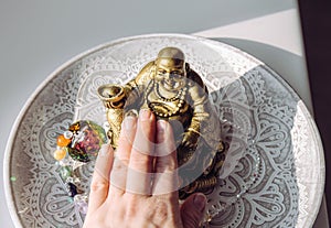 Person hand rubbing small golden laughing Buddha figurine tummy.
