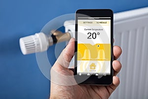 Person Hand Setting Temperature Of Thermostat Using Mobilephone