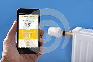 Person Hand Setting Temperature Of Thermostat Using Mobilephone