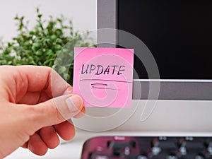 Person hand sticking a pink paper notes with the reminder Update on to a monitor at an office workplace