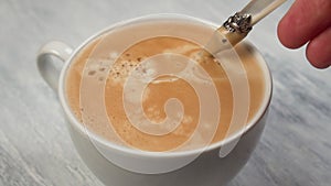 Person hand stirring coffee with spoon in white cup on gray textured wooden table.