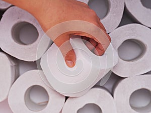 A person hand taking a toilet roll from heap of toilet paper rolls