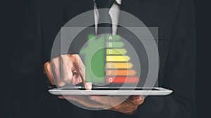 Person hand using digital tablet with house icon energy efficiency scale image on dark background, Concept of ecological and bio