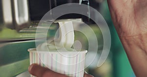 Person, hands and ice cream swirl with machine for sweet desert, sundae or food in a cup. Closeup of vanilla serving