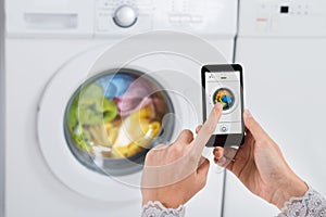 Person Hands Operating Washing Machine With Mobile Phone