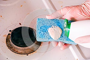 Person hands with sponge and cleaning solution ready to clean dirty gas stove