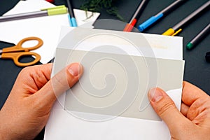 Person hands taking out gray paper from envelope with office supplies