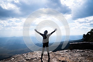 A person hands up standing on rocky mountain looking out at scenic natural