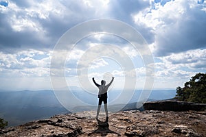 A person hands up standing on rocky mountain looking out at scenic natural view