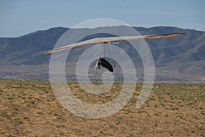 Person hang gliding above the field on the mountainous landscape