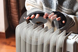 Person heating their hands at home over a domestic portable radiator in winter