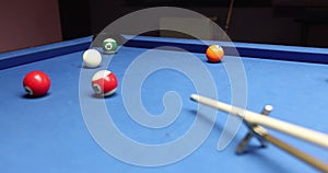 Person hits white ball leaning above blue pool table