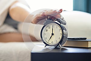 Person hitting snooze on a classic alarm clock