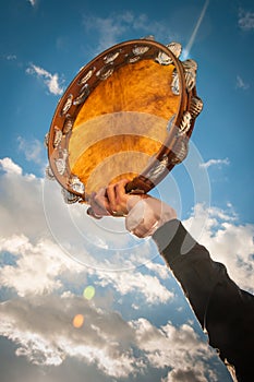 Person holding aloft a tambourine against blue sky