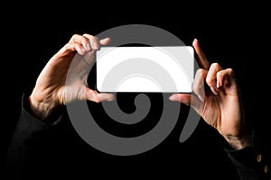 Person holding in both hands mobile phone horizontally with blank white screen, isolated on black background