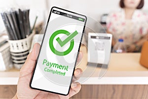 A person holding a cell phone with a green check mark on it that says payment completed