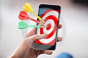 Person Holding Cellphone With Darts On Target
