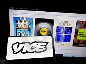 Person holding cellphone with logo of broadcasting company Vice Media LLC on screen in front of business webpage.