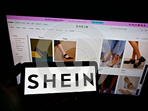 Person holding cellphone with logo of Chinese e-commerce company Shein on screen in front of business webpage.
