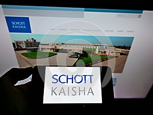 Person holding cellphone with logo of Indian packaging company Schott Kaisha Pvt Ltd on screen in front of business webpage.