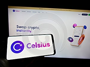 Person holding cellphone with logo of US crypto company Celsius Network LLC on screen in front of business webpage.