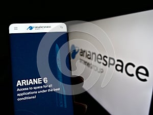 Person holding cellphone with webpage of French aerospace company Arianespace SAS on screen in front of logo.