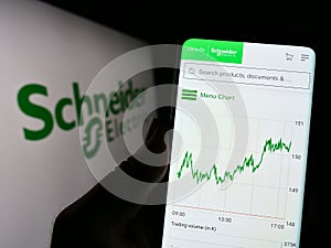 Person holding cellphone with website of French company Schneider Electric SE on screen in front of logo.