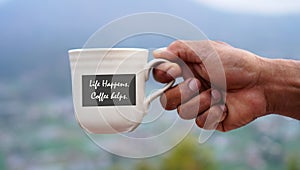 Person holding a cup of tea or coffee with inspirational text quote on it - Life happens. Coffee helps. With man drinking morning photo