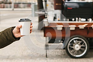 The person is holding a disposable glass in his hand with coffee or another hot drink.