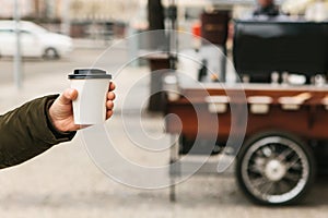 The person is holding a disposable glass in his hand with coffee or another hot drink.