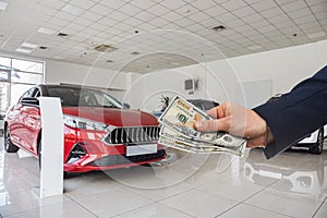 Person holding dollar money in the hands stands front car at modern showroom