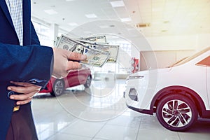 Person holding dollar money in the hands stands front car at modern showroom