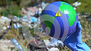 Person holding Earth globe with warning sign against open dumping background