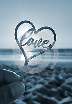 Person holding finger hand stick shape heart word Love background sea Blue color