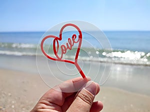 Person holding in fingers hand stick in shape red heart and word Love