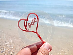 Person holding in fingers hand a stick in shape of red heart and word Love
