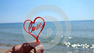 Person holding fingers hand stick shape red heart word Love background sea